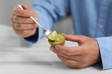 Man eating kiwi with spoon at white table, closeup