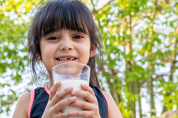 Close-up portrait of her. She drinks a glass of cold milk after playing outside her house.