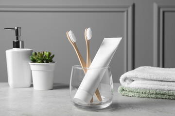 Fototapeta na wymiar Bamboo toothbrushes in holder, toothpaste, houseplant and towels on light grey table