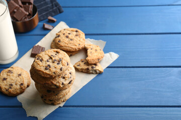 Tasty chocolate chip cookies and glass of milk on blue wooden table. Space for text