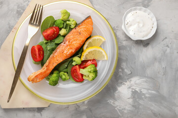 Healthy meal. Piece of grilled salmon, vegetables, lemon and spinach served with sauce on light grey textured table, flat lay. Space for text
