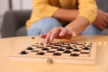 Fototapeta premium Woman playing checkers at wooden table, closeup