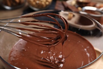 Chocolate cream flowing from whisk into bowl on table, closeup