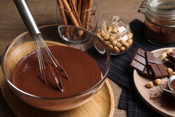 Bowl of chocolate cream with whisk and ingredients on wooden table