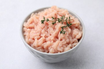Fototapeta na wymiar Fresh raw minced meat and thyme in bowl on light grey table, closeup