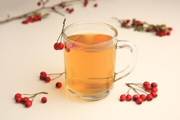 Cup with hawthorn tea and berries on beige table