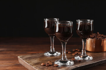 Shot glasses with coffee liqueur and beans on wooden table, space for text