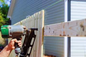 Air nail gun is used by man to nail planks together to create wooden fence around his yard