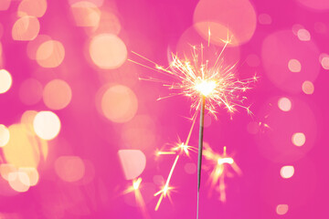 Beautiful Christmas sparkler on pink background with blurred lights