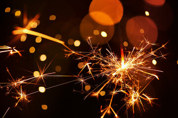 Beautiful Christmas sparkler on black background with blurred lights, closeup