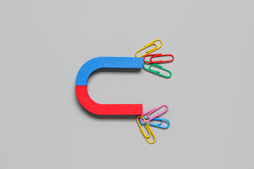 Magnet attracting paper clips on grey background