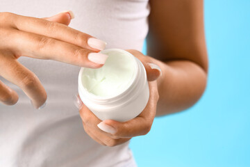 Pretty young woman with jar of cream on blue background, closeup