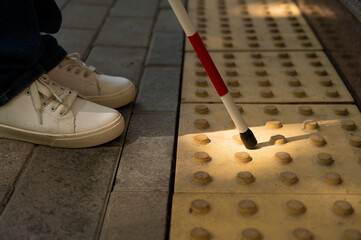 A close-up of a woman's feet with a tactile cane and a tactile tile indicating an obstacle.