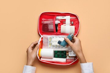 Female hands with first aid kit and pills on beige background