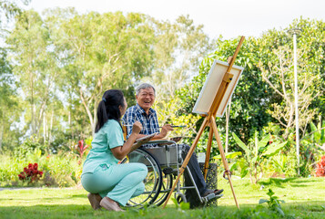 Naklejka na ściany i meble Back of Asian nurse woman sit near senior man on wheelchair enjoy to paint the painting outdoor in the garden and they look happiness with laughing together.
