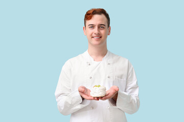 Male confectioner in uniform with Pavlova cake on blue background