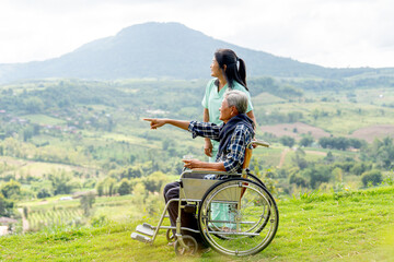 Asian nurse stand and look to the direction of senior man on wheelchair pointing and both stay near...