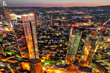Die Skyline von Frankfurt am Main mit Hochhäusern und Straßenzügen der Innenstadt aus der Luft in der Dämmerung mit künstlicher Strassenbeleuchtung