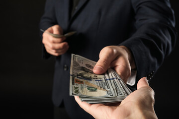 Young businessman giving bribe on dark background, closeup