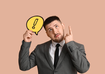 Young businessman holding speech bubble with exclamation mark and pointing at something on beige background. Business idea concept