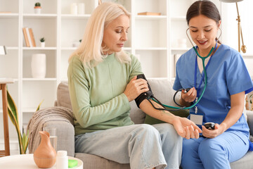 Female doctor measuring blood pressure of patient at home