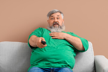Mature man watching TV on sofa against beige background