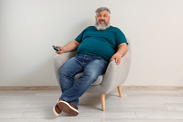 Mature man watching TV in armchair near light wall