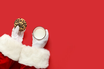 Obraz na płótnie Canvas Santa Claus hands with glass of milk and cookie on red background