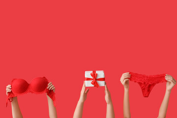 Female hands with sexy underwear and Christmas gift on red background - obrazy, fototapety, plakaty