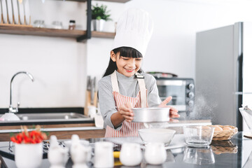 Little asian girl with chef hat and apron cooking in kitchen for homemade bake cake at home