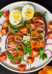toast with smoked salmon, onion and vegetables on a white plate close up