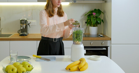 Teen girl making a spinach and banana smoothie on kitchen - Powered by Adobe