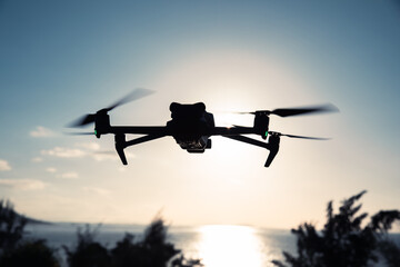 Silhouette of flying drone which taking photo over sunrise sea