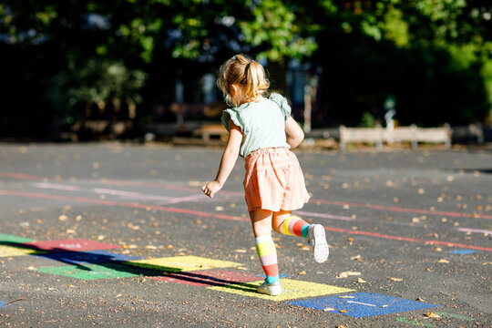 Cute little toddler girl playing hopscotch game drawn with colorful chalks on asphalt. Little active child jumping on playground outdoors on a sunny day. Summer activities for children.