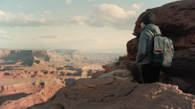 Female hiker walks to the edge of a cliff and admires stunning canyon views during sunset