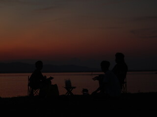 Fototapeta na wymiar Silhouette of young men sitting by the lake enjoying the sunset. peaceful atmosphere in nature