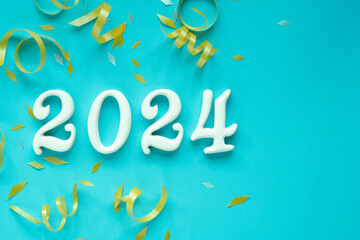 close up number 2024 shape wood on blue color background with gold rolling ribbon and confetti for happy new year and countdown party concept