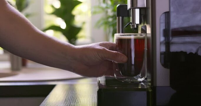 Male hand picking up a cup of coffee prepared by a coffee machine at home