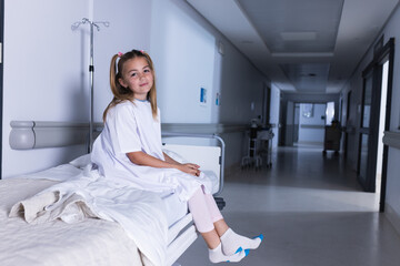 Caucasian girl sitting on bed in hospital corridor with copy space