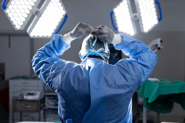Back of african american female doctor wearing face mask in hospital operating room - Powered by Adobe
