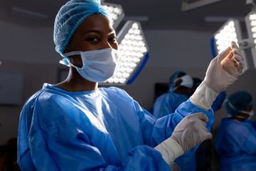 African american female doctor with face mask wearing protective gloves in hospital operating room