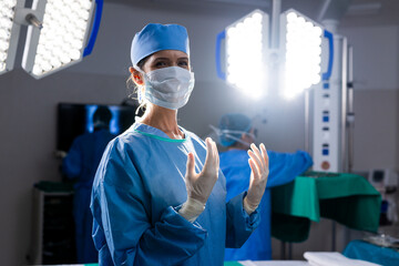Portrait of caucasian female doctor with face mask and protective gloves in hospital operating room