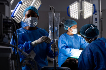 Diverse female doctors with face masks doing surgery in hospital operating room