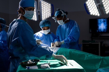 Diverse female doctors with face masks doing surgery in hospital operating room - obrazy, fototapety, plakaty