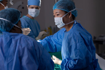 Diverse female doctors with face masks doing surgery in hospital operating room
