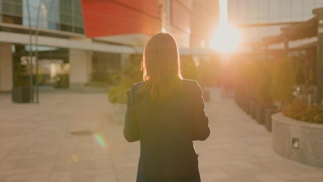 Sunrise Serenity back view of a A young business woman embraces the dawn, confidently navigating city streets with elegance and professionalism in a mesmerizing rear view tracking shot.