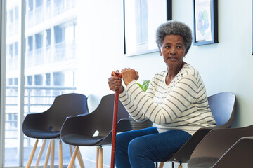 African american senior woman with walking stick sitting in hospital waiting room