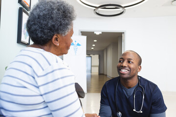 Happy african american male doctor talking with senior woman in hospital waiting room