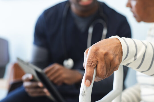 African american male doctor using tablet and talking with senior woman in hospital waiting room