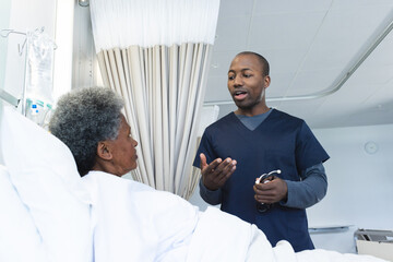 African american male doctor talking with senior female patient in hospital room